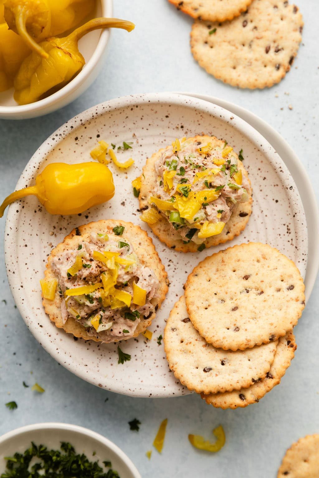 Overhead view of a plate filled with crackers topped with Tuna Salad and a pickled pepper on the side.