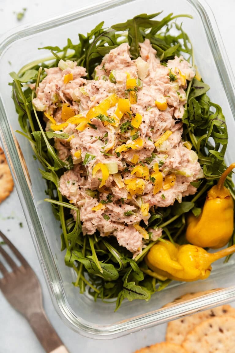 Overhead view of a glass meal prep container filled with arugula and topped with Tuna Salad.