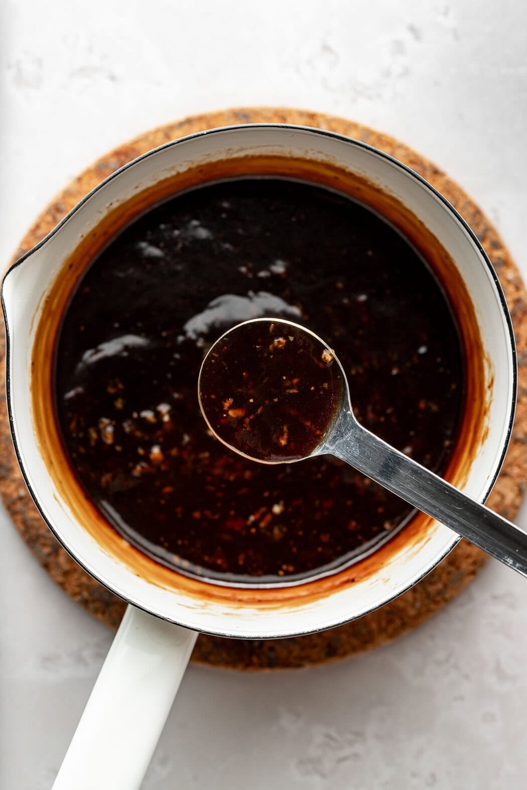 A measuring spoon lifting a scoop of teriyaki sauce from a bowl.