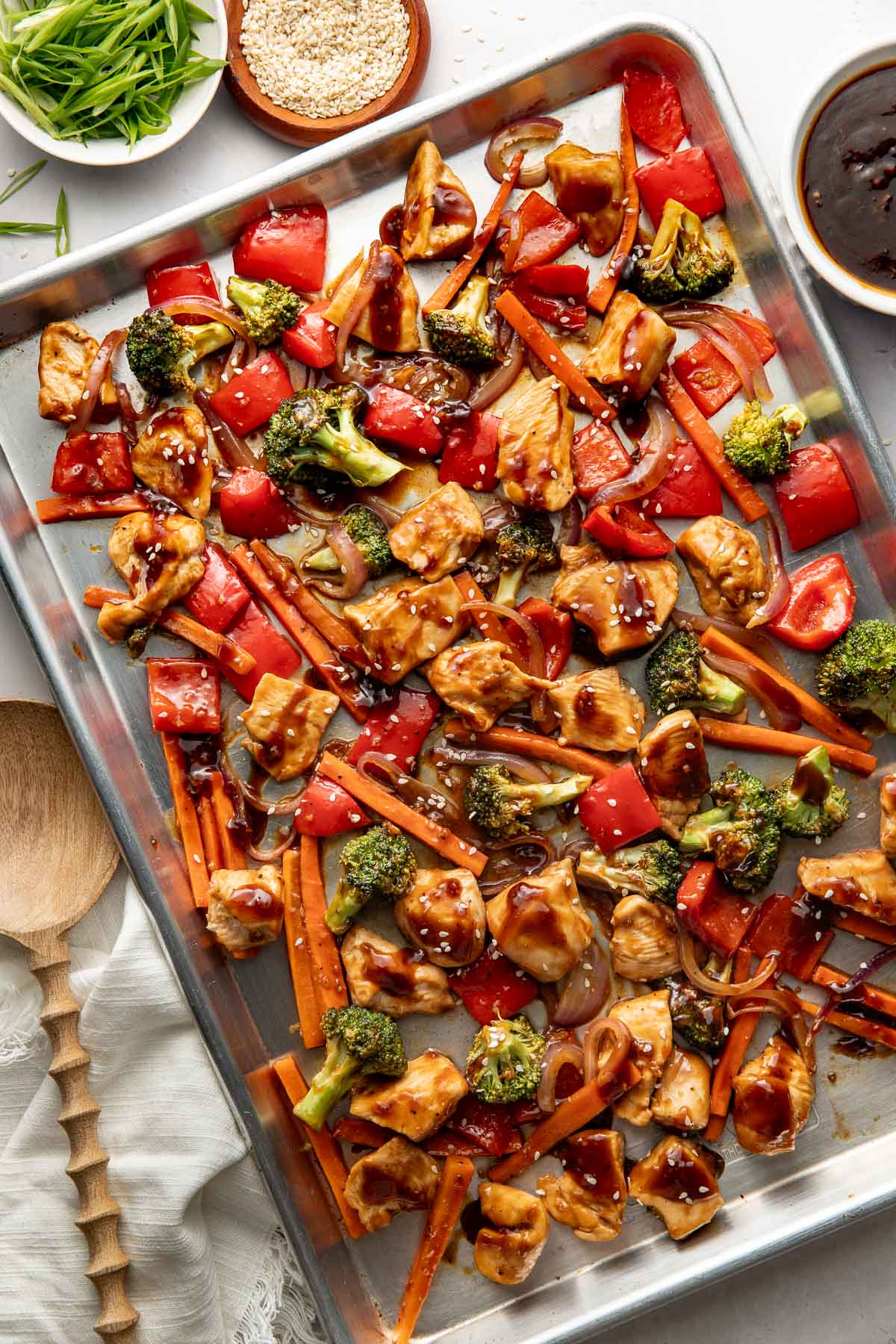 Baked sheet pan teriyaki chicken and vegetables topped with a drizzle of teriyaki sauce and white sesame seeds.