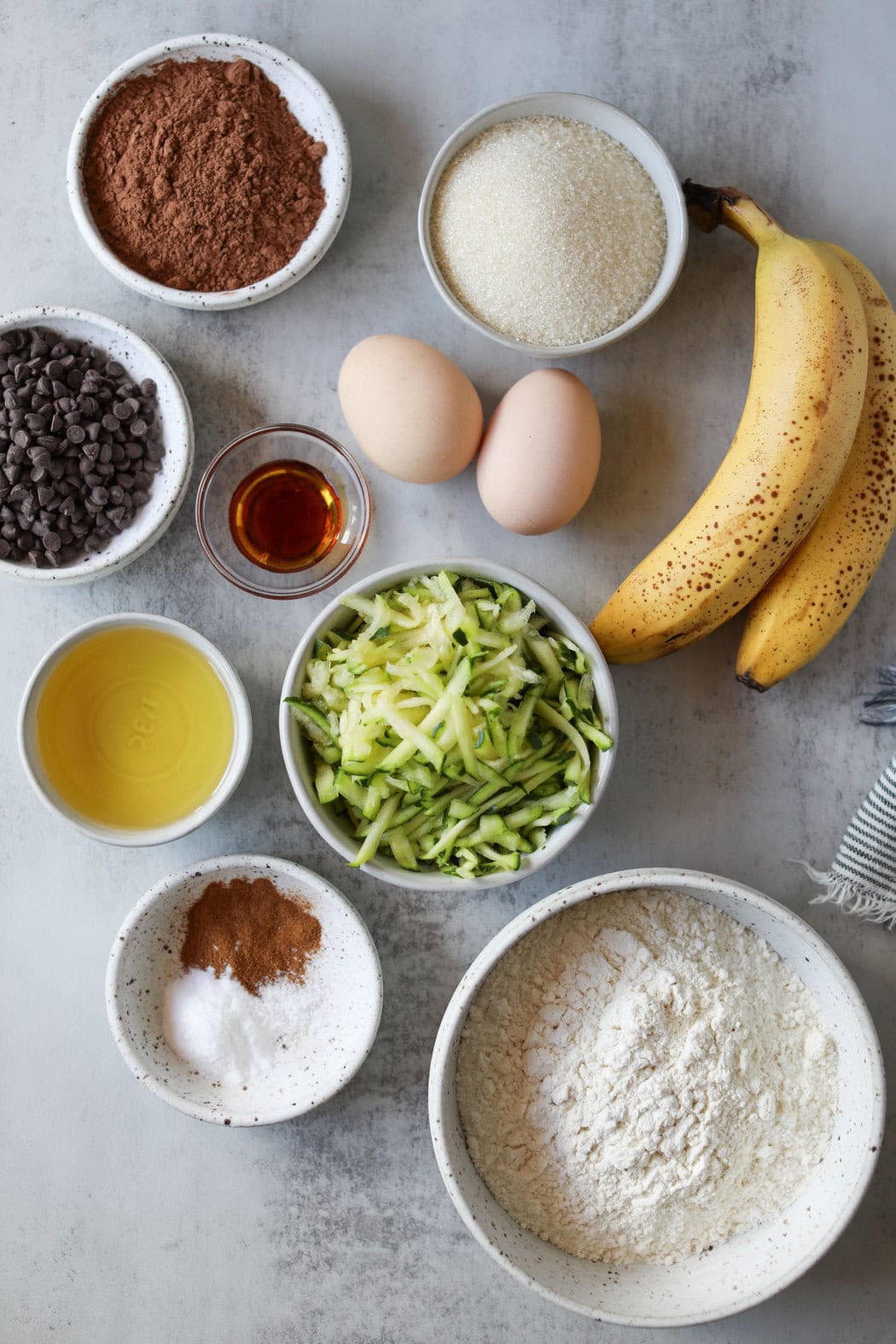 Overhead view of a variety of ingredients for Double Chocolate Zucchini Muffins in different sized bowls. 