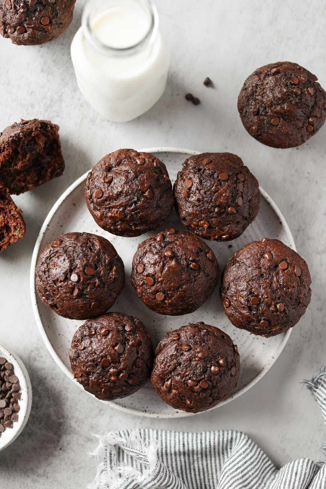 Overhead view of a freshly baked plate of Double Chocolate Zucchini Muffins with cold milk beside them. 