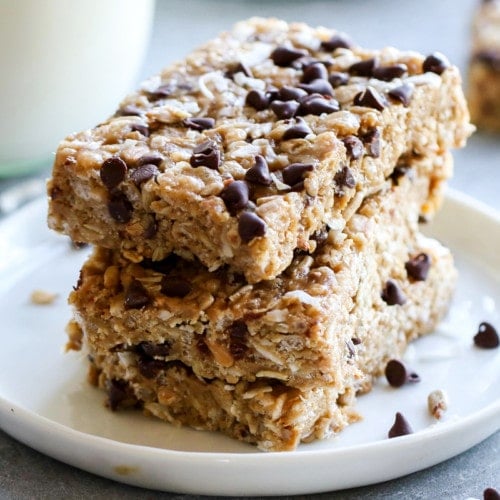 Three homemade clif bars with chocolate chips and coconut stacked up on a white plate