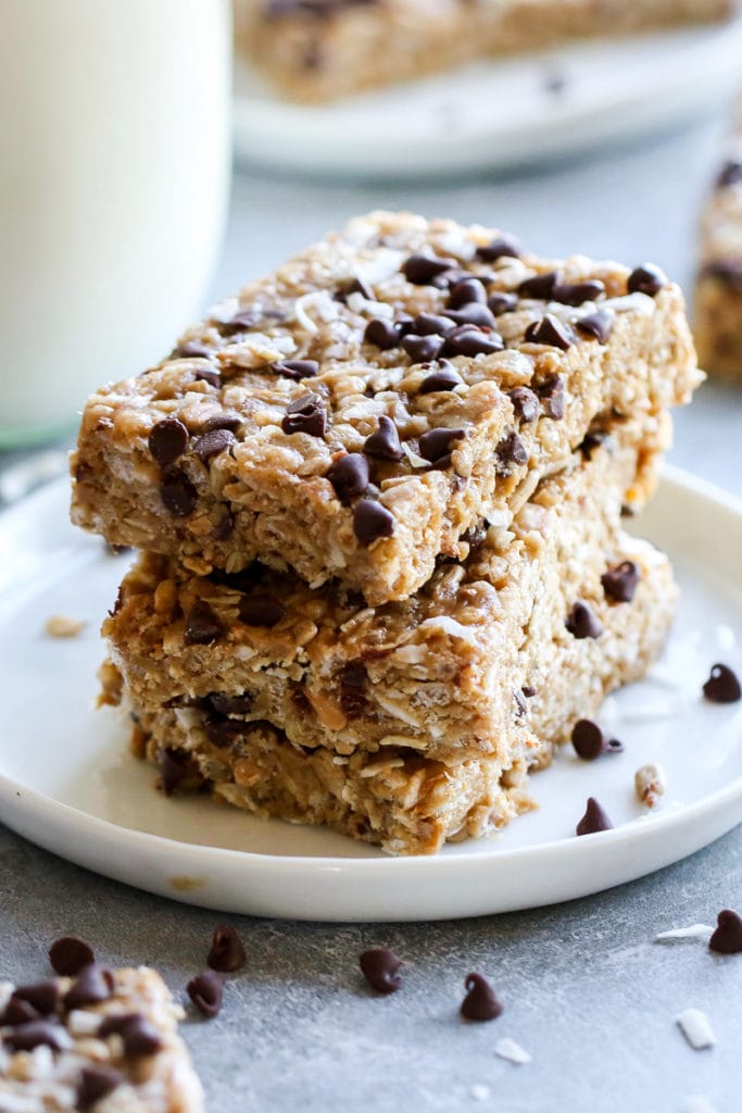 Three homemade clif bars with chocolate chips and coconut stacked up on a white plate