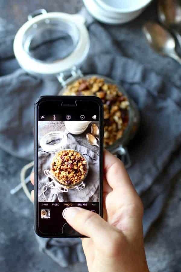 Iphone being held to take a picture of pumpkin spice granola in a canister jar