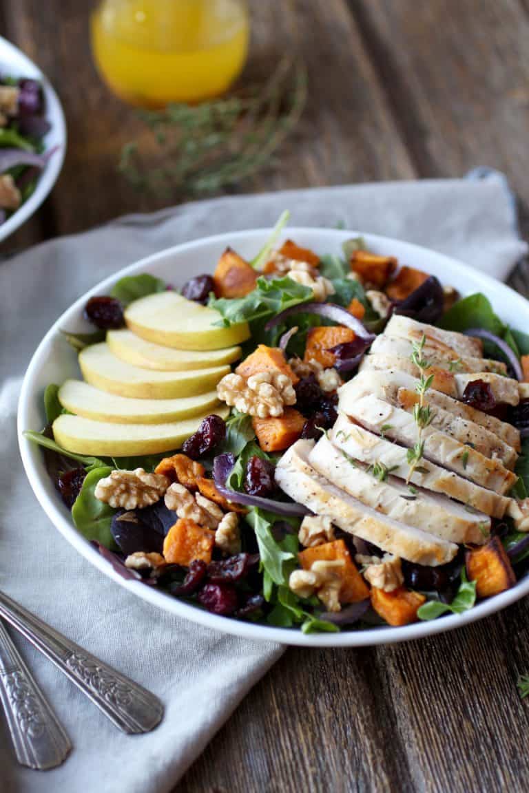 Close up view of a plate of Harvest Chicken salad topped with walnut pieces and apple slices. 