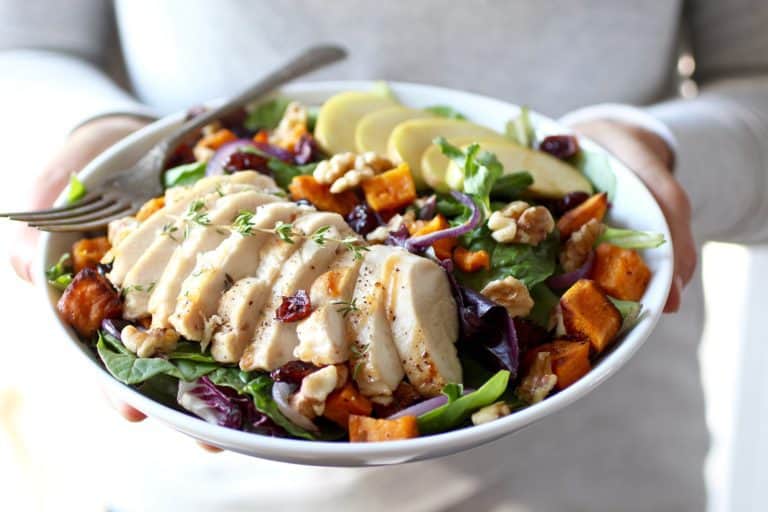 A plate full of Harvest Chicken salad with roasted sweet potato, cranberries, red onion, apples, pecans and goat cheese drizzled with a simple citrus vinaigrette. 