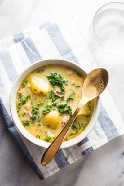 Aerial view of Slow Cooker Zuppa Toscana in a white bowl with a gold spoon on top