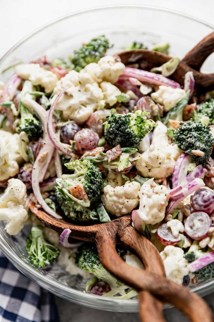 Close up view of creamy broccoli cauliflower salad with bacon in serving bowl with a twisted handle wooden spoon.