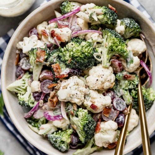 Creamy Broccoli Cauliflower Salad in a serving bowl with gold serving utensils.