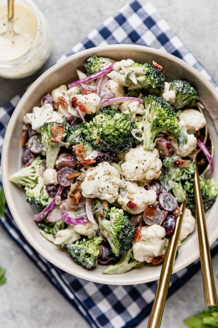 Overhead view broccoli cauliflower salad in white bowl, topped with bacon