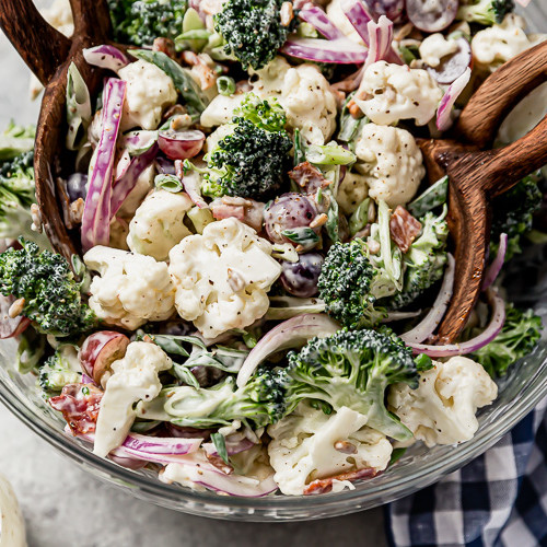 Overhead view of broccoli cauliflower salad with bacon crumbles served in a clear mixing bowl with a twisted wooden handle.