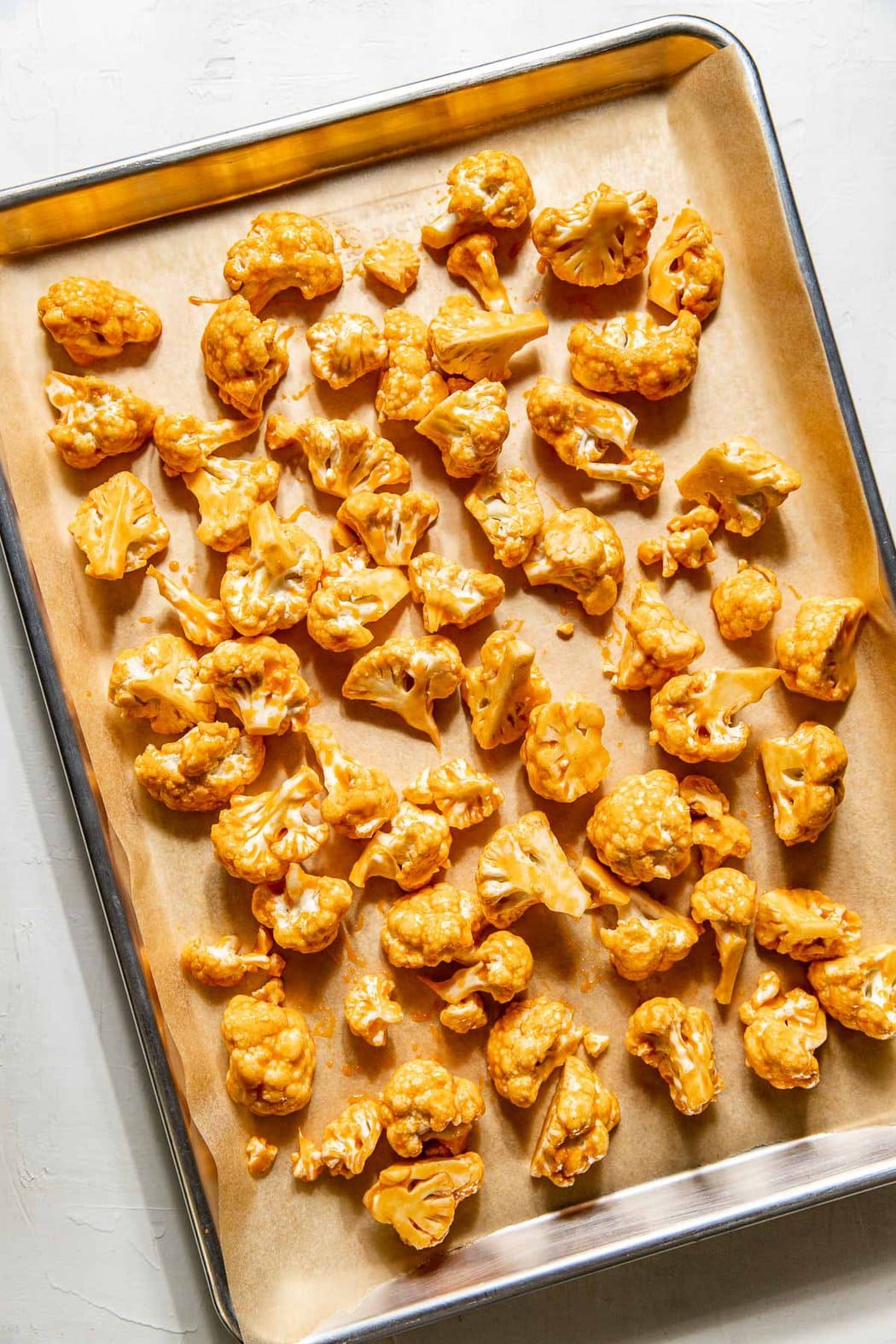 Overhead view of a sheet pan filled with cauliflower pieces coated in buffalo sauce. 