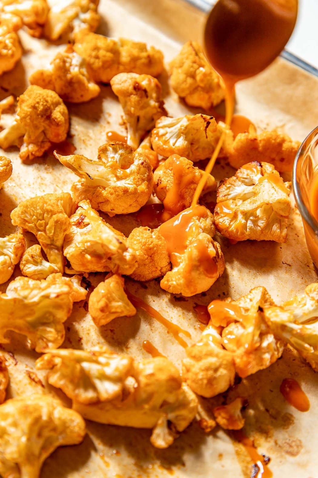 Close up view of cauliflower pieces on a sheet pan being coated in buffalo sauce. 