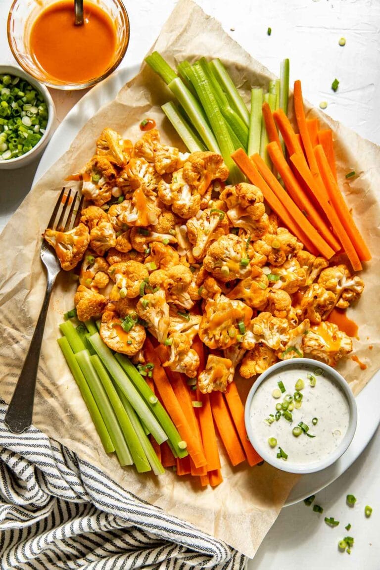 Overhead view of a platter of buffalo cauliflower bites surrounded by sliced carrots and celery sticks with a side of ranch.