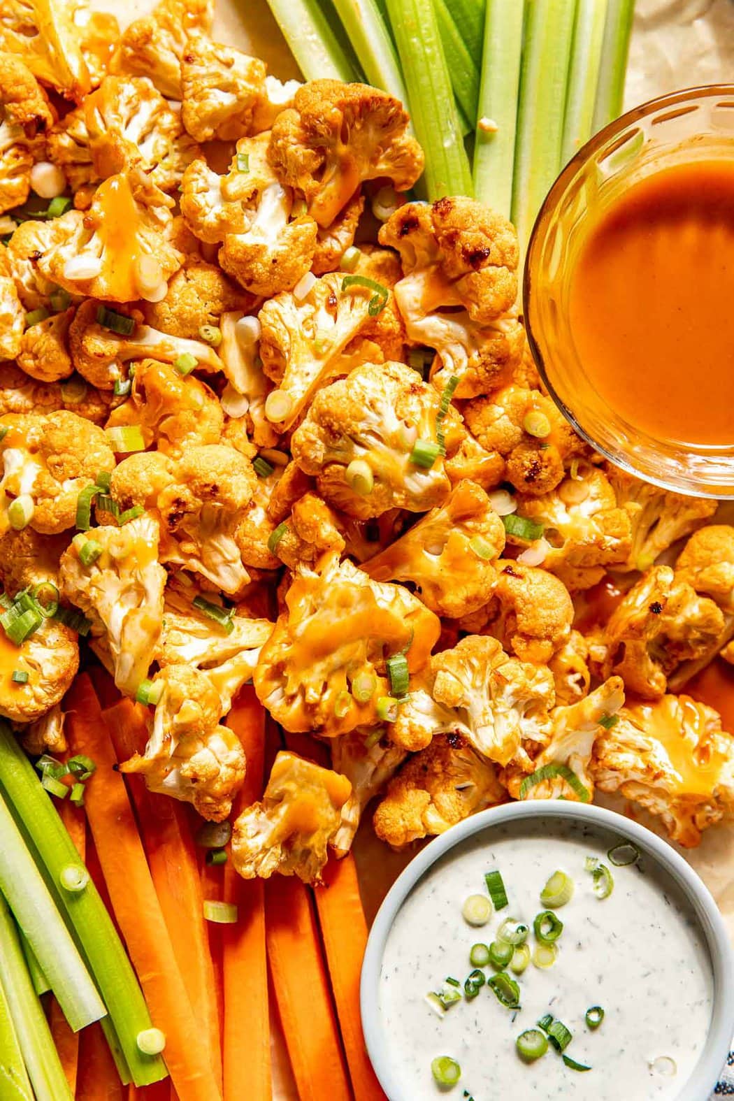 Overhead view of a pan of freshly roasted Buffalo Cauliflower Bites with buffalo sauce, ranch, carrots and celery sticks. 