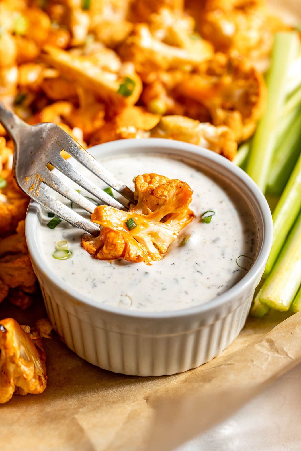 Close up view of a piece of a Buffalo Cauliflower bite being dipped into a ranch sauce. 