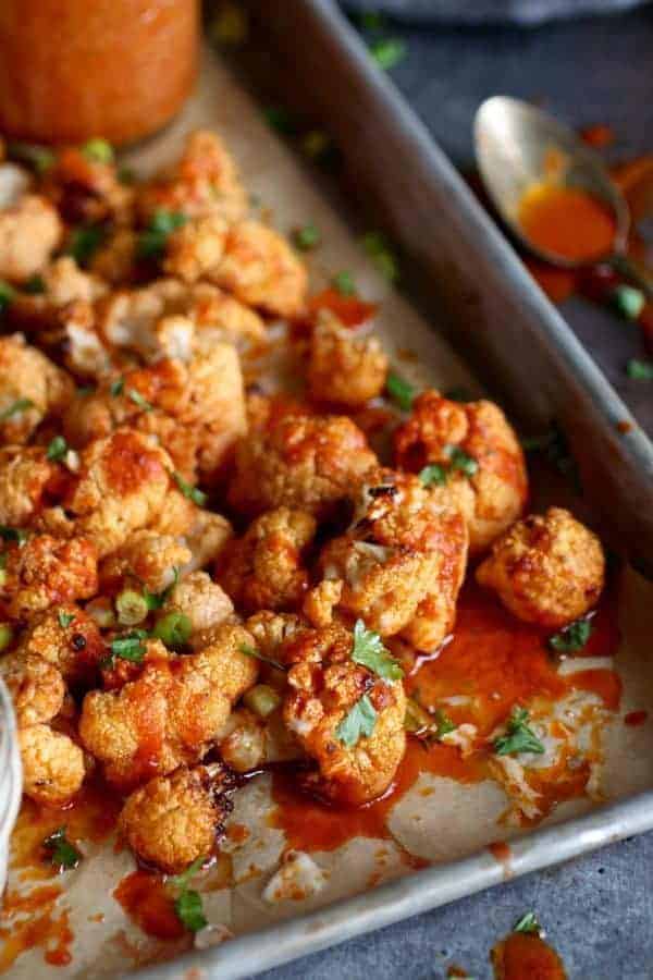 Cauliflower buffalo bites on a baking sheet topped with homemade buffalo sauce.