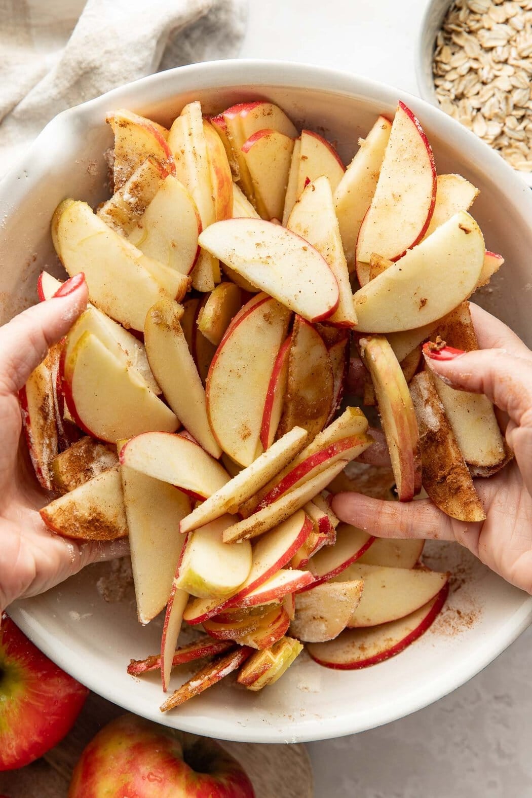 Hands tossing sliced apples with spices in a bowl.