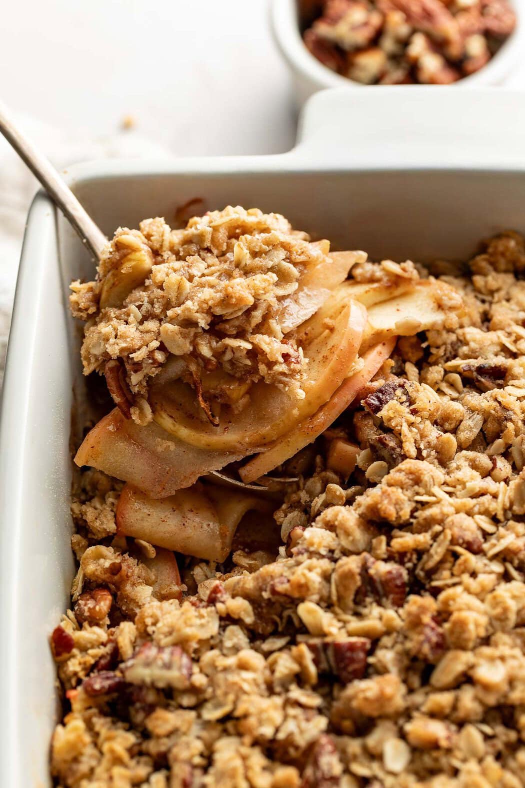 A spoon lifting a scoop of healthy apple crisp from a baking dish.