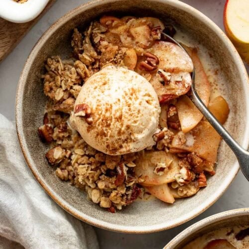 A bowl of healthy apple crisp topped with a scoop of ice cream, a spoon sticking out.