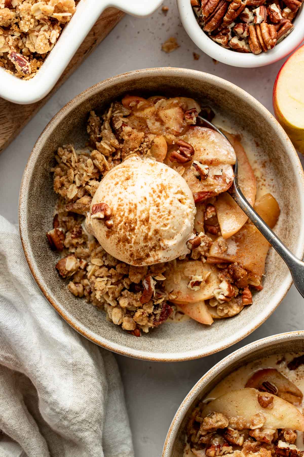 A bowl of healthy apple crisp topped with a scoop of ice cream, a spoon sticking out.