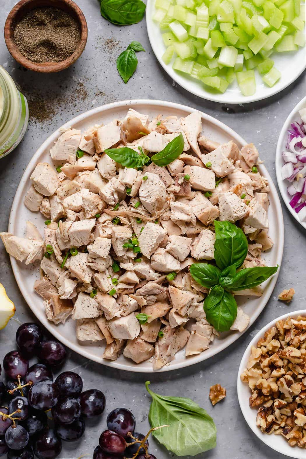 Overhead photo of the ingredients for Waldorf Chicken Salad including cubed chicken topped with fresh basil. 