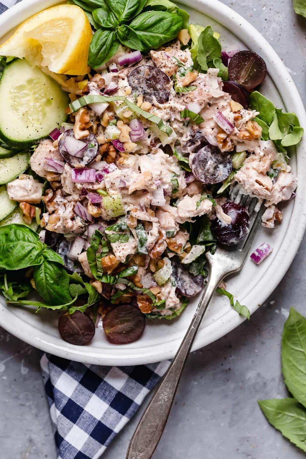 Overhead photo of Classic Waldorf Chicken Salad on a white plate served on top of greens along with cucumber slices, lemon wedge and fresh basil. 