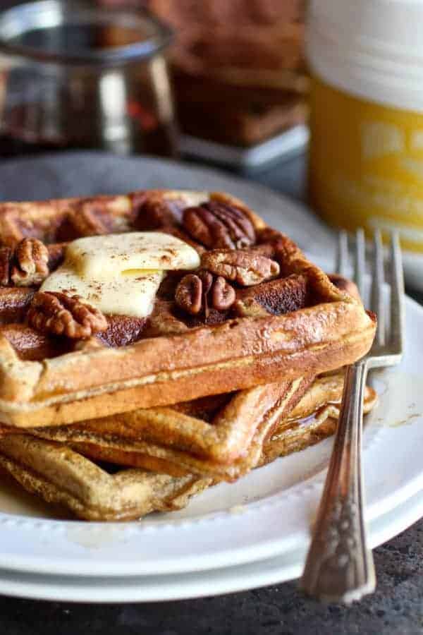 Three Paleo Pumpkin Spice Protein Waffles stacked on a white plate with a fork on the side of the plate