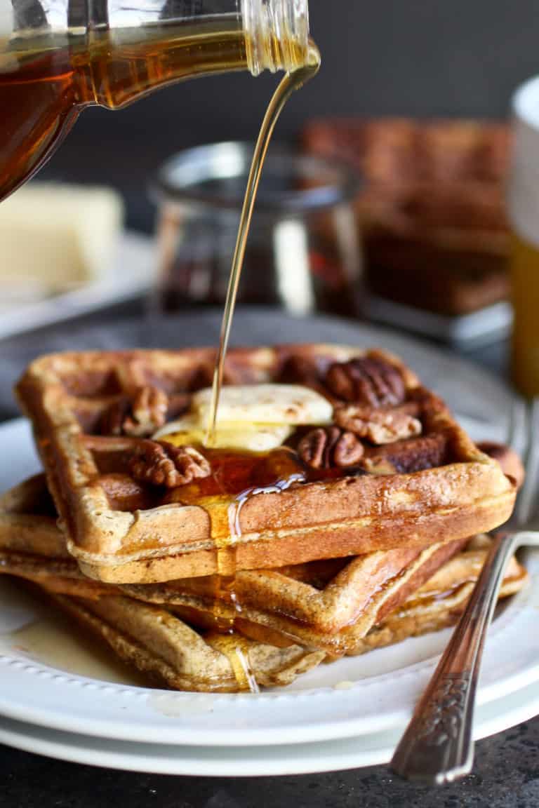 A plate of Pumpkin Spice Protein Waffles being drizzled with maple syrup. 