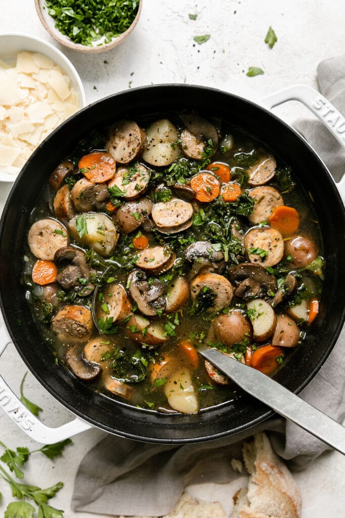 A large Dutch oven filled with Harvest Italian soup with sausage and kale, ladle in soup.