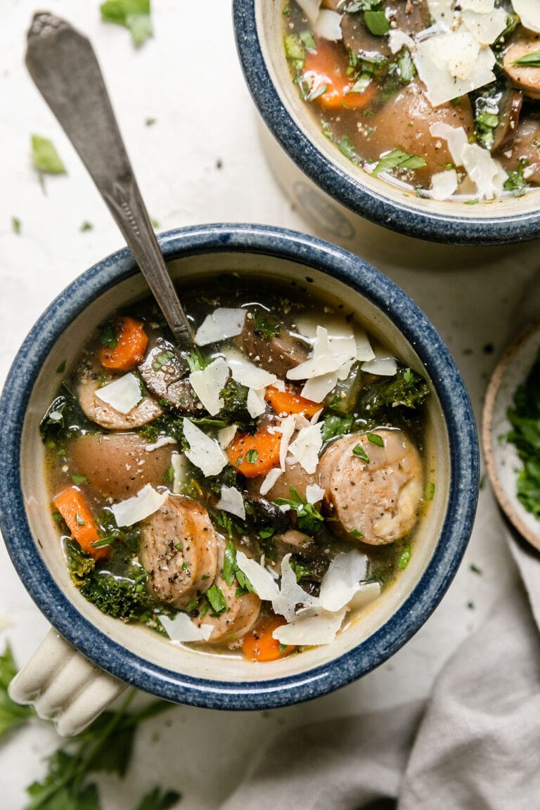 Overhead view of a ceramic bowl filled with Italian soup with sausage and topped with shaved parmesan. 