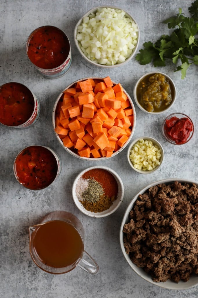 Overhead view of all ingredients for slow cooker sweet potato chili arranged in small bowls and cans.