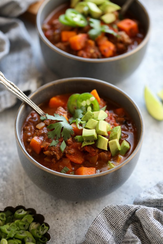 Slow cooker sweet potato chili in a grey bowl topped with avocado, jalapeno, and cilantro.