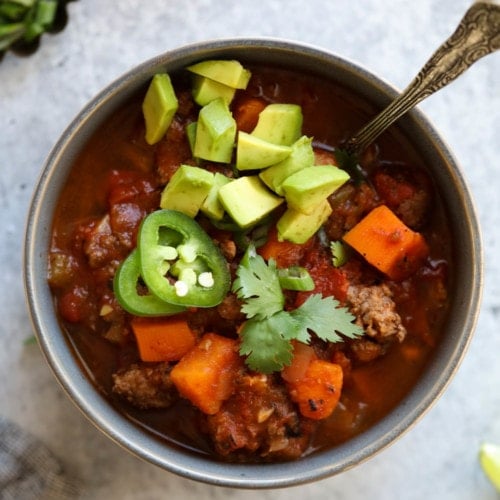 Overhead view of slow cooker sweet potato chili in a grey bowl topped with avocado and fresh cilantro.