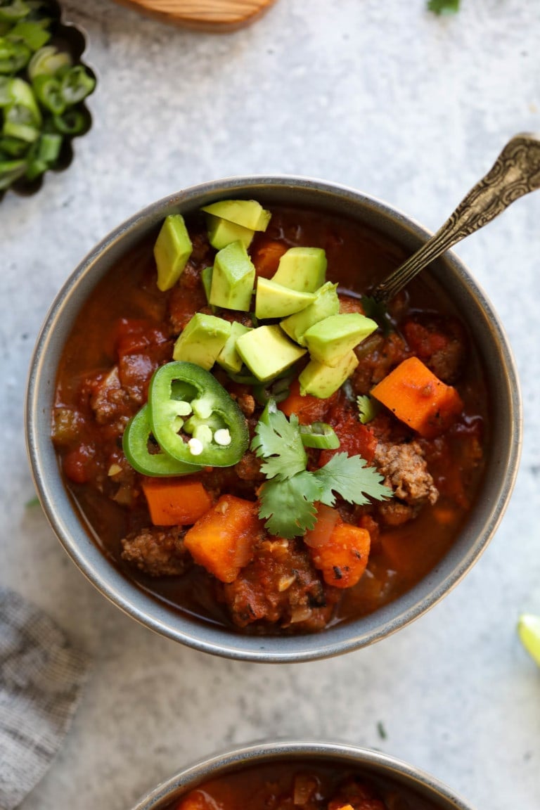 Overhead view blue bowl filled with sweet potato chili, topped with diced avocado and jalapeño slices