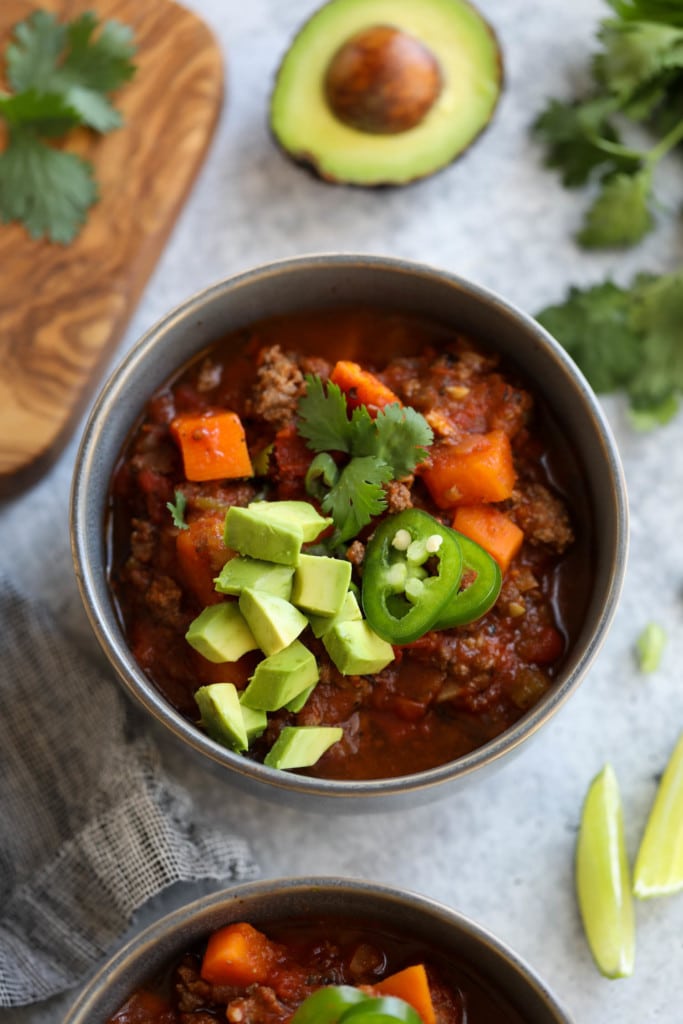 A bowl filled with chunky slow cooker sweet potato chili topped with jalapeno slices, diced avocado, and fresh cilantro.