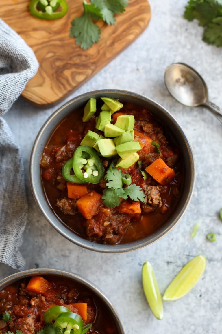 Overhead view of two bowls of sweet potato chili topped with cilantro, jalapeno, and avocado.