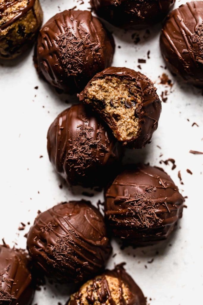 Several chocolate coated chocolate chip cookie dough bites arranged together, topped with chocolate shavings. 