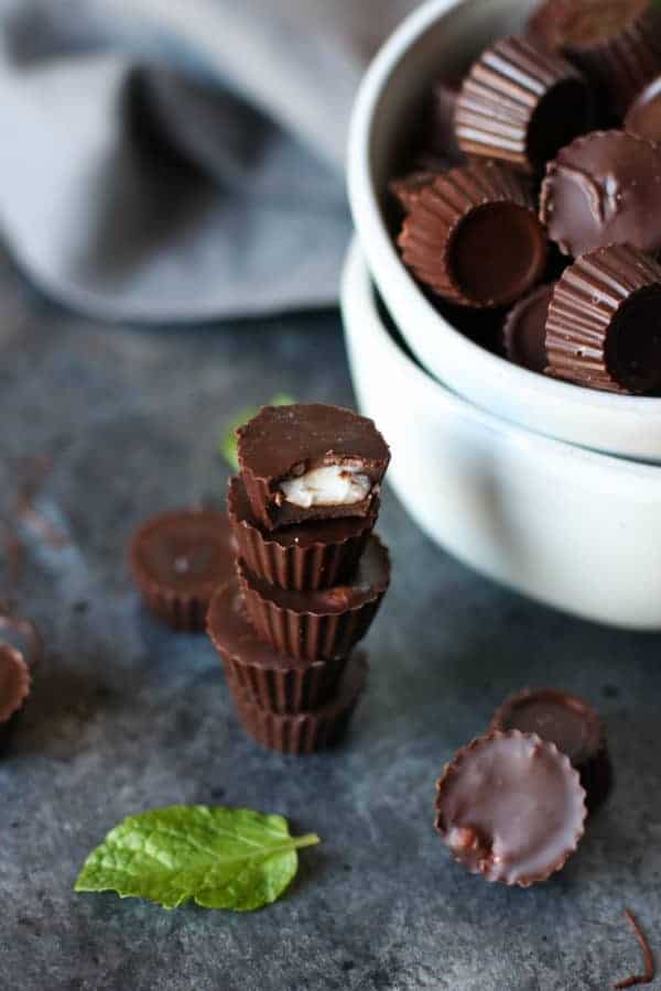 3-Ingredient Dark Chocolate Mint Cups stacked besides a white bowl full of mint cups