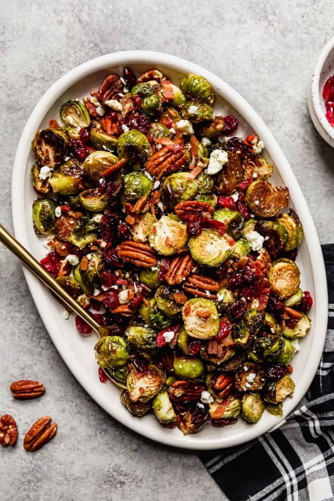  Roasted Brussel Sprouts with Bacon and Balsamic on a white serving platter with a gold serving spoon.