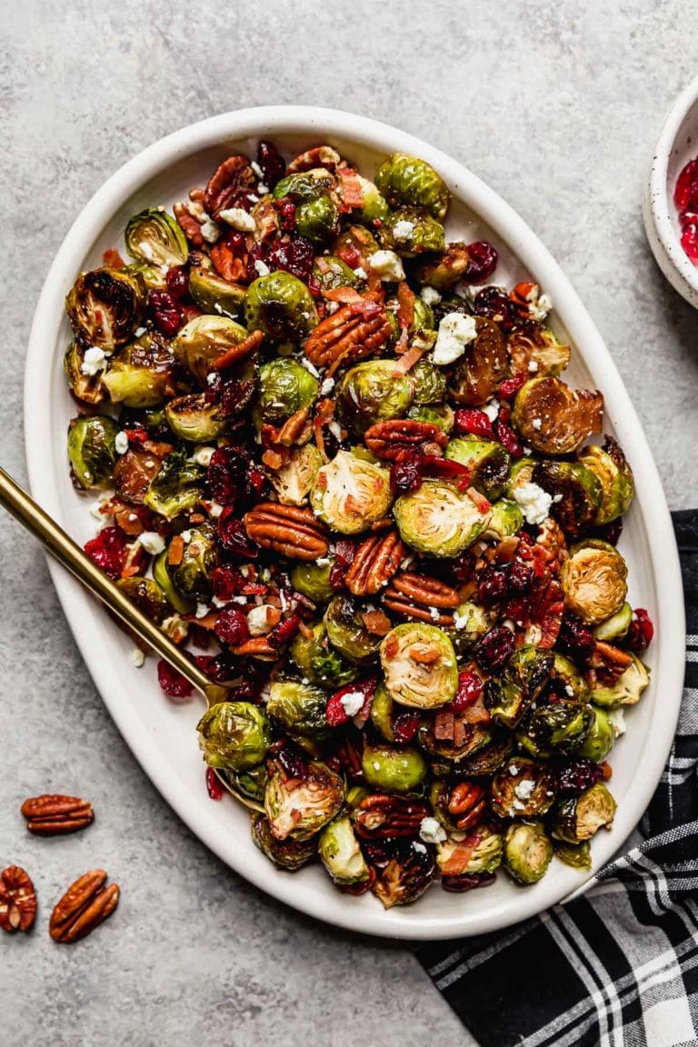 Overhead view Roasted Brussels sprouts with pecans, cranberries and feta cheese crumbles on a white serving tray.