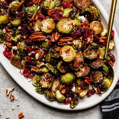 Roasted brussels sprouts with bacon and dried cranberries on a white serving platter