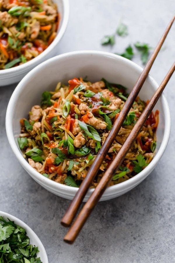 Egg roll in a bowl made with pork, veggies, and scallions in a white bowl with chopsticks on the side