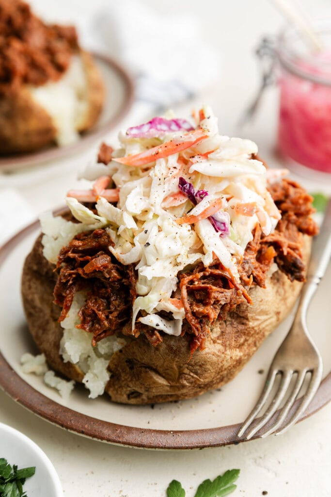 Close up side view baked potato stuffed with shredded bbq beef and topped with coleslaw