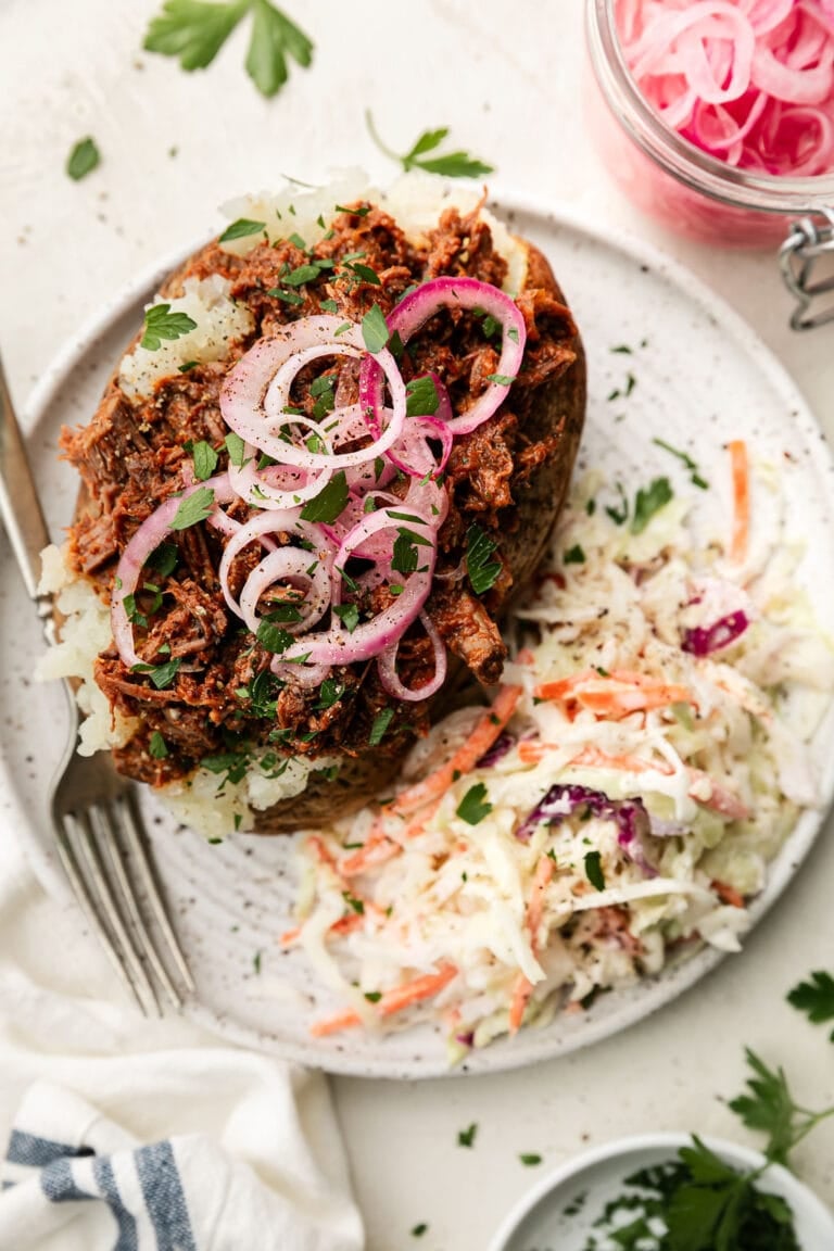 Overhead view of BBQ Beef and coleslaw on a white plate topped with red onions and fresh herbs and seasonings. 