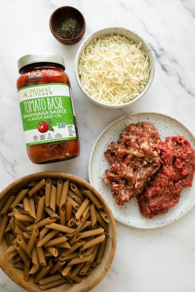 All ingredients for 5-Ingredient Baked Ziti arranged together in small bowls with the marinara sauce in a Primal Kitchen jar.