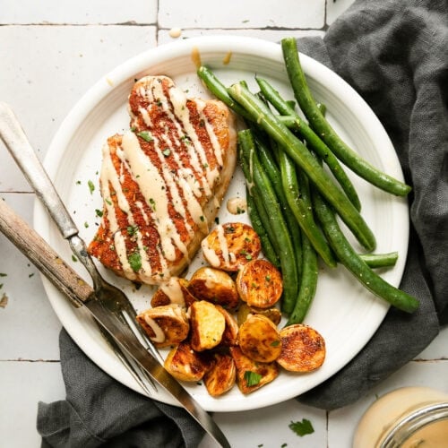 Overhead view serving of sheet pan honey mustard pork chop on plate with side of roasted potato halves and green beans.