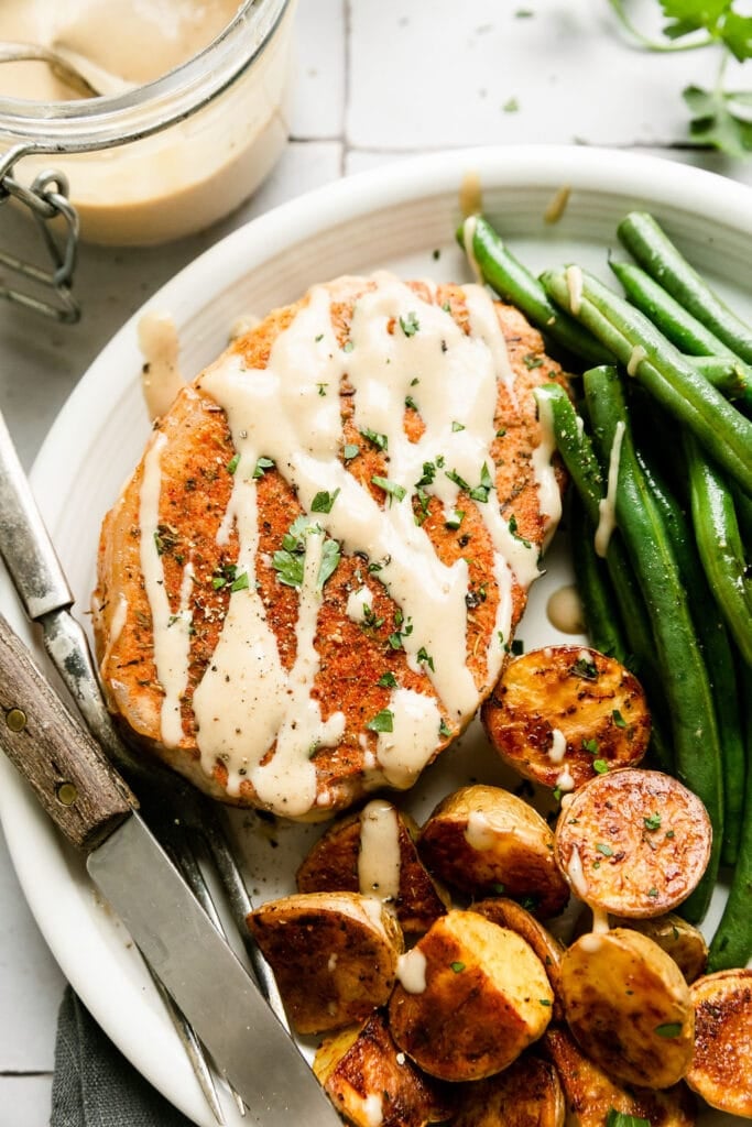 Overhead view white plate with serving of sheet pan honey mustard pork chop, roasted green beans, and potato halves.