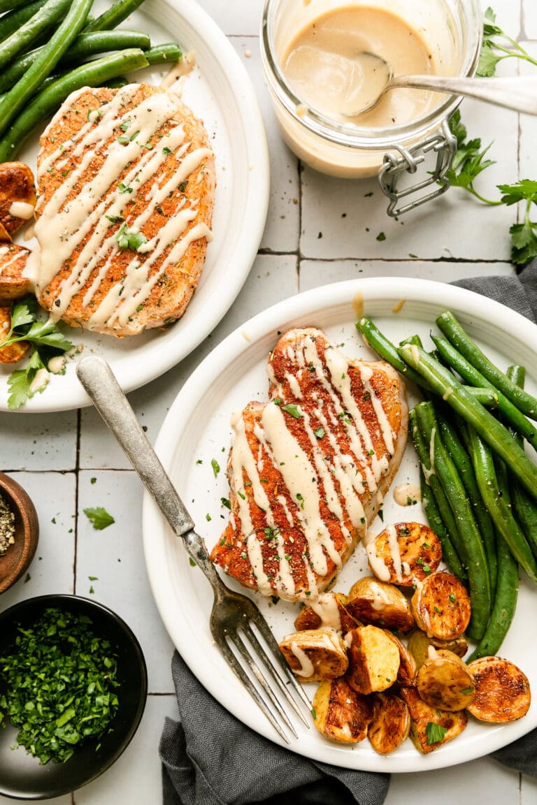 Overhead view of two plates of honey mustard pork chops served with roasted potatoes and green beans all drizzled with honey mustard sauce.
